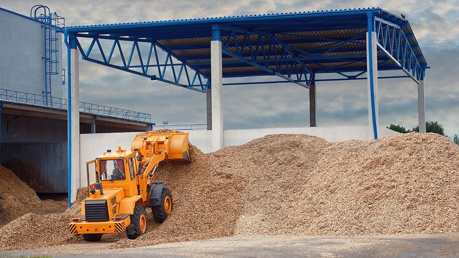 Front loader loading wood chips in pile in warehouse. Loader works at wood chips storage yard. Alternative ecological fuels. Sawdust processing, woodchip biomass heap. Pellets manufacturing.