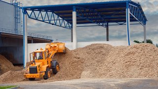 Front loader loading wood chips in pile in warehouse. Loader works at wood chips storage yard. Alternative ecological fuels. Sawdust processing, woodchip biomass heap. Pellets manufacturing.