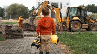 Child with excavator near construction site, dreams to be an engineer. Little builder. Education, and imagination, purposefulness concept