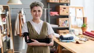 Young successful female tailor with partial arm standing against her workplace