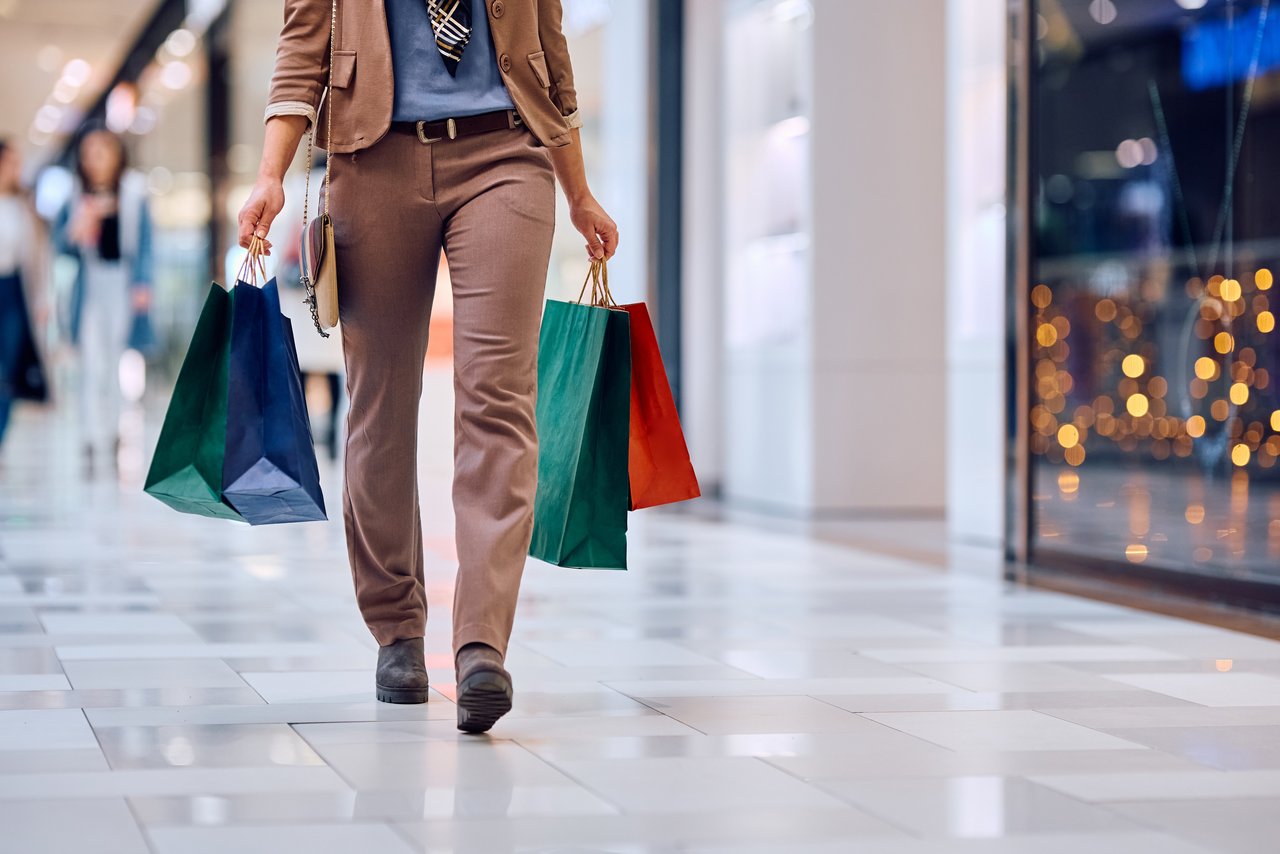 Unrecognizable woman with shopping bags walks through mall.