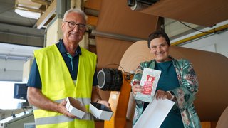 ernd Langer, früherer Geschäftsführer und heute beratend tätig, und Daniela Müller, zuständig für Marketing und Vertrieb, zeigen Verpackungen, die mit Erzeugnissen der Roti Verpackungsdruck GmbH beschichtet sind.