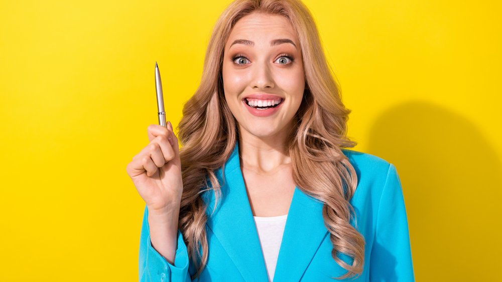 Photo of cheerful clever lady hand hold point pen toothy smile bright idea isolated on yellow color background